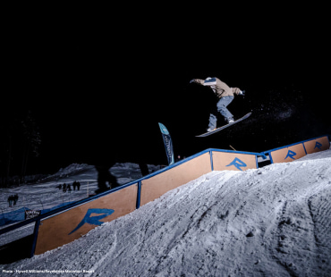 Snowboarder mid air about to hit the rail at night