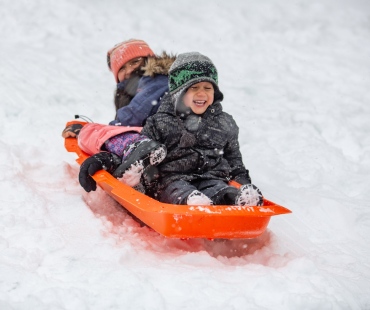 2 children sliding down hill on sled