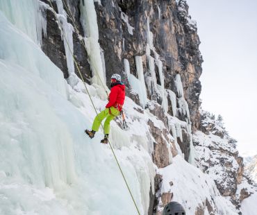 person ice climbing up frozen waterfall