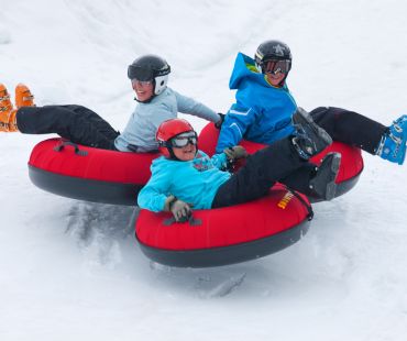 3 People riding tubes down snowy trails