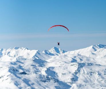 Person paragliding over the snow covered mountains