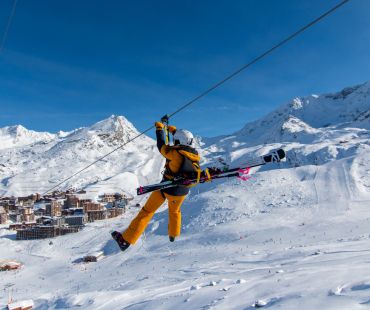 Person flying down zipline with snowy mountain scenery